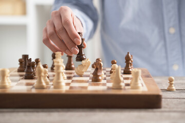 Girl player performs a knight chess piece move. On the chessboard there is a brown board made of natural wood. A female hand holds a horse figure.
