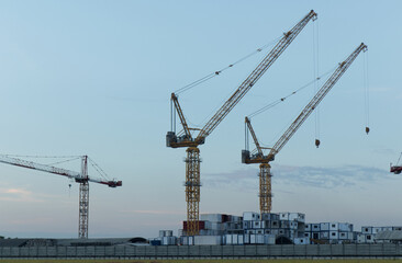Fototapeta na wymiar White containers, yellow steel tower cranes, near green fields,