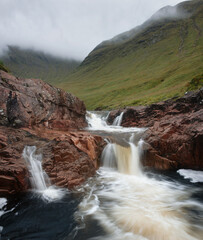 Fototapeta na wymiar Small mountain river with waterfalls and mountains covered with clouds. River Etive, Highlands, Scotland