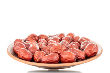 Several sweet dried ziziphus berries on a clay dish, close-up, isolated on white.