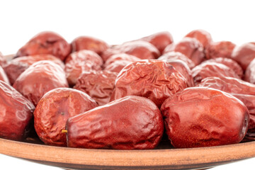 Several sweet dried ziziphus berries on a clay dish, close-up, isolated on white.