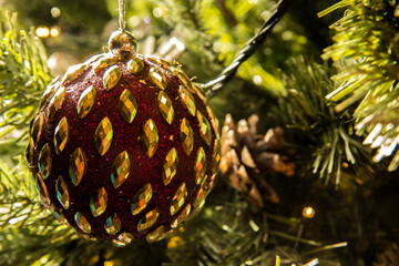 Detail of a red decorative ball hanging from an artificial Christmas tree.