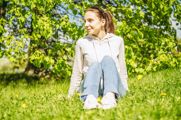 Naklejka na ściany i meble happy young lady enjoying spring green nature, harmony and freedom concept. Beauty girl sitting on green grass in a meadow. Spring nature