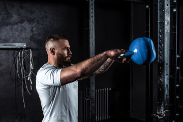 Young active strong sweaty muscular fit man with big muscles doing kettlebell swing workout cross...