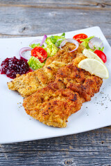 Traditional deep-fried schnitzel with green salad, tomatoes and cranberry jam served as close-up on...