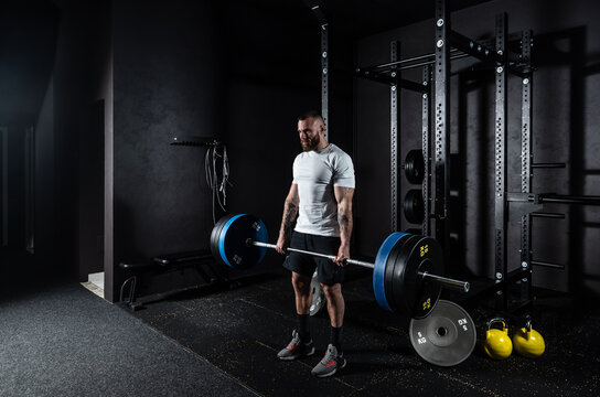 Young active strong sweaty muscular fit man with big muscles doing hardcore deadlift or weightlift workout cross training with heavy barbell weights in the gym. Male sportperson strength lifting 