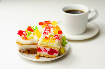 A portion of cream cake with pieces of colorful jelly and sprinkled with coconut flakes
