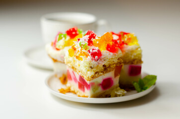 A portion of cream cake with pieces of colorful jelly and sprinkled with coconut flakes