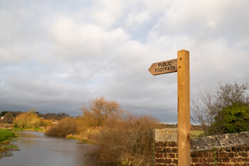 Wooden public footpath sign indicating public access along the bank of the River Bure in the Norfolk village of Buxton