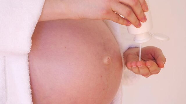 Pregnant woman squeezes the jar of Moisturizer on the hand and spreads the body cream on the belly, anti stretch marks, protection and prevention of stretchmarks during maternity video
