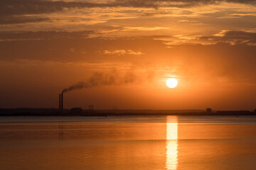 Sunset view of smoking industrial pipes on a horizon over the river.