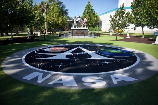 Kennedy Space Center, Florida, USA: Project Apollo insignia, Bronze statue of Apollo 11 astronauts, and Moon Tree Garden descended from seeds taken to moon at Apollo and Saturn V Center. 