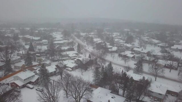 Aerial drone view of a residential neighborhood during a winter snowstorm.
