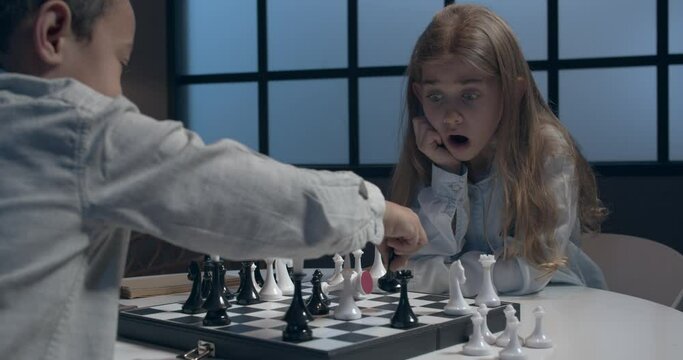 Little children playing chess at home in evening