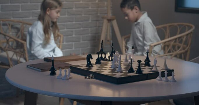 Little children playing chess at home in evening, focus on table with chessboard