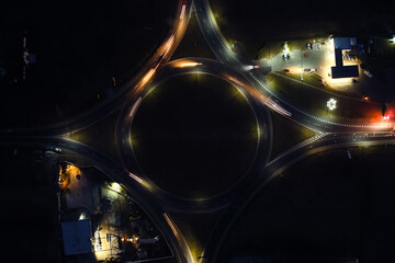 Aerial view of road roundabout intersection with fast moving heavy traffic at night. Top view of urban circular transportation crossroads. Rush hour with blurred car trail lights