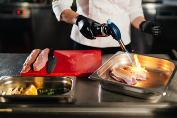 The chef is frying the meat in the plate with the help of burner and preparing for cutting meat.