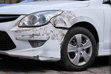 Dented car with damaged fender parked on city street side. Road safety and vehicle insurance concept