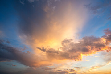 Dramatic cloudscape with puffy clouds lit by orange setting sun and blue sky