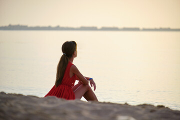 Lonely young woman sitting on ocean sandy beach by seaside enjoying warm tropical evening