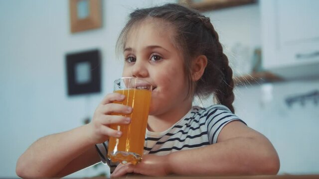 little girl child drinking juice. healthy eating a child eating breakfast kid dream concept. daughter girl in kitchen drinks juice and licks her lips. positive kid smiling having breakfast orange