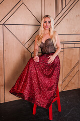 A girl in a beautiful red dress sits on a chair
