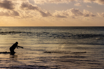 Silhouette of fisherman throwing his net at sunset in Fernando de Noronha, Brazil.
