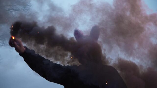 scary evil maniac in a rabbit mask looks at the camera and holds colored smoke. a crazy man stands in the forest and is illuminated by police flashers. arrest of the killer with grenades of smoke