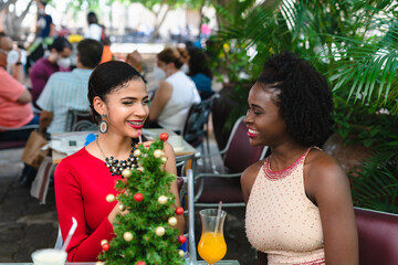 two young latin women in elegant dresses sitting outside drinking