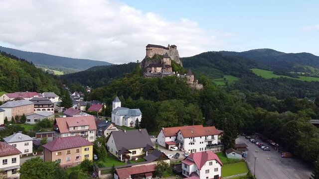 Flying over small settlement in mountains with old castle in the center. Green coniferous forest around. Aerial View of Orava Castle in Slovakia.