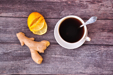 Ginger root, lemon slices and a cup of black tea on a wooden table.
