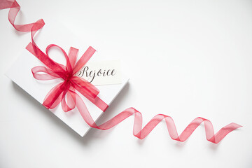 On original Christmas themed photograph of a white gift with a red ribbon curled and flowing out of the image with a tag that says Rejoice - Powered by Adobe