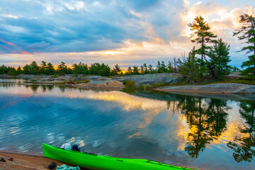 Sunset seen  on a rocky campsite on Georgian Bay, Ontario Canada with a green kayak in the...