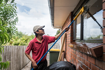 Man washing window with long pole and brush outdoors in Auckland