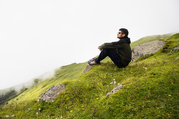 Young traveling man wearing Googles and sitting on the top of the mountain cliff with relaxing mood...