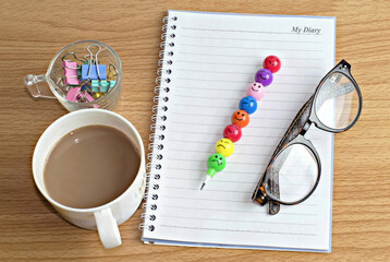 Diary book,glasses,pen,paper clip and beverage malt drink on wooden table.