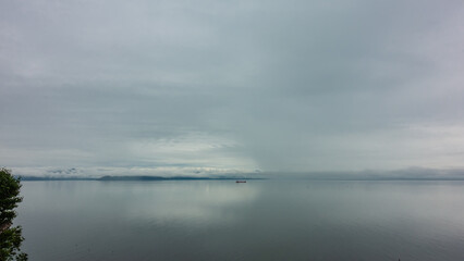 A foggy day on the Pacific Ocean. A tiny silhouette of a ship is visible on the smooth water. Cloudy sky. Reflection. Pastel shades. Copy space. Petropavlovsk-Kamchatsky