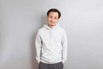 Fototapeta premium Confident asian man in a hoodie standing on grey background.