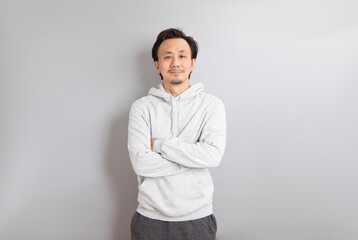 Fototapeta premium Confident asian man in a hoodie standing on grey background.
