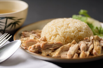 Hainanese chicken rice with coriander, cucumber and chicken soup on black background. Local food in East and Southeast Asia