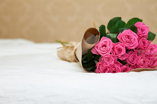 Beautiful bouquet of pink roses in a wrapper lies on a white bed. A gift to a loved one. Decorating your home.