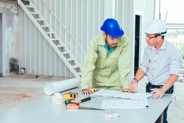 Engineer and worker looking home plans with helmet, craftsman tool and home model on workplace at construction site.