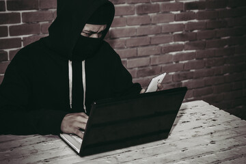 Anonymous hacker using laptop and smartphone for stealing personal data from internet.