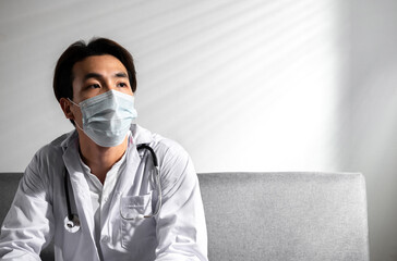 Depressed Young Asian male doctor with surgery face mask in a medical coat Overworked having a mental health breakdown during covid-19 outbreak. Medical and coronavirus Stress and frustration concept