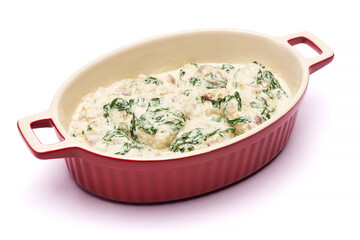 Delicious meatballs with spinach in a creamy sauce in baking dish on white background