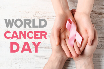 Hands with pink ribbon on light wooden background. World Cancer Day