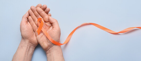 Fototapeta Male hands with orange ribbon on light background. Kidney cancer and leukaemia awareness concept obraz