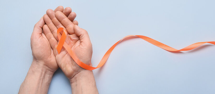Male hands with orange ribbon on light background. Kidney cancer and leukaemia awareness concept