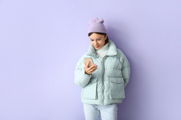 Pretty young woman in stylish warm clothes and with phone on color background