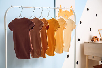 Rack with hanging baby bodysuits near color wall in children's room